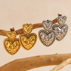 Vintage Herz-Ohrringe in Gold und Stahl mit Hammerschlag-Textur auf Holzzweig