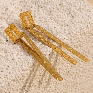 Gros plan sur des boucles d'oreilles barres en plaqué or avec texture sur pierre blanche
