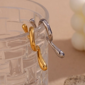 Detail von minimalistischen Fluid Drop Ohrringen in Gold und Silber auf Glasrand