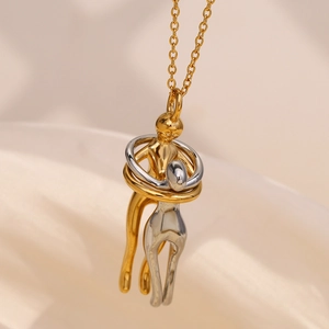 Macro view of gold and silver lovers hugging pendant on elegant beige silk fabric