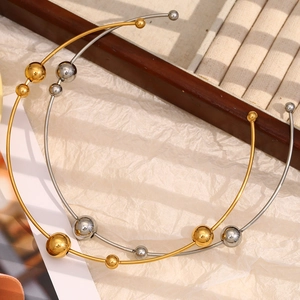 Dettaglio di girocolli minimalisti placcati oro 18K e argento con sfere metalliche su carta