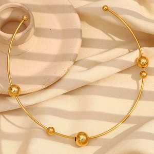 Dettaglio del girocollo minimalista in oro con cinque perle lucide su tessuto beige