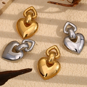 Boucles d'oreilles cœur polies en finition or et argent sur fond de pierre beige