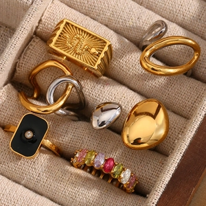 Detailed view of various gold and silver snake rings with gemstones on a beige texture