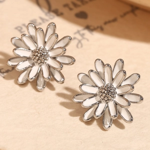 Gros plan de boucles d'oreilles marguerites en émail blanc sur une carte vintage