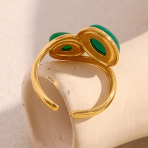Detail of a gold-plated open ring featuring two green emerald-style stones on a light stand