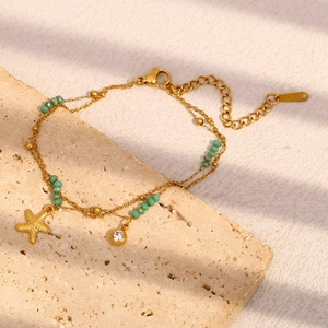 Detail eines 18K vergoldeten zweilagigen Seestern-Armbands mit grünen Perlen auf Steinplatte