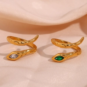 Close-up of gold snake rings with emerald and white marquise zircons on beige silk