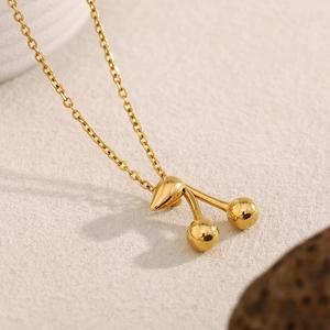 Dettaglio macro di una collana con ciondolo a ciliegia placcata oro 18K su pietra sabbiosa