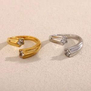 Detalle de anillos de estrella dorados y plateados con circonitas en fondo beige