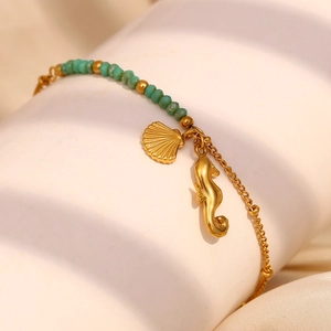 Détail de breloques hippocampe et coquillage plaqués or 18K sur bracelet en perles vertes