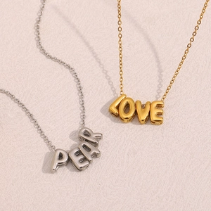 Détail de colliers en acier doré 18K et argent avec pendentifs lettres LOVE et PEAR