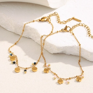 Detail of 18K gold-plated bracelets featuring clover charms and polished beads on white stone