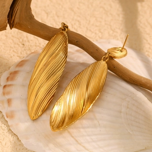 Macro shot of long golden petal drop earrings with fine radial grooves on sand background