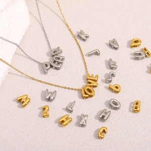 Colliers avec pendentifs lettres évidées en or 18 carats et argent sur surface texturée
