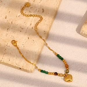 Macro detail of 18K gold-plated stainless steel bracelet with green beads and heart charm