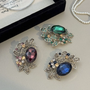 Macro detail of vintage olive leaf brooches in emerald green, burgundy, and navy blue