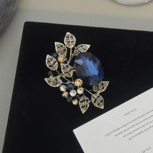 Detailed close-up of a vintage leaf brooch with deep blue gemstone on black velvet