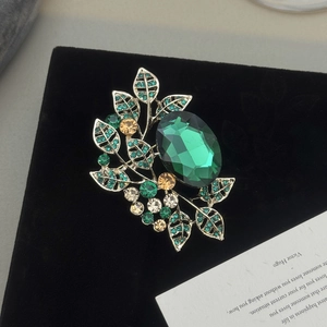 Macro shot of olive leaf brooch with green gemstone on elegant black velvet background