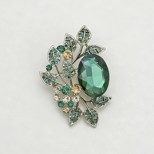 Detailed close-up of retro olive leaf brooch with green gemstone and sparkling crystals