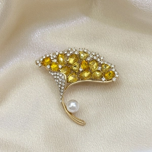 Detailansicht einer goldenen Ginkgoblatt-Brosche mit gelben Kristallen und weißer Perle