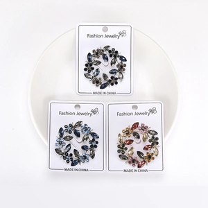 Détail de trois broches couronne d'olivier en cristal avec strass colorés sur des cartes