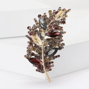 Detailed view of leaf-shaped brooch featuring colorful rhinestones on a white pedestal