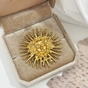 Vintage gold sun goddess relief brooch displayed on beige velvet with antique paper