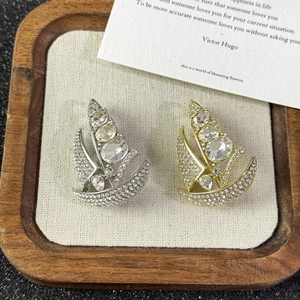 Detailed close-up of gold and silver sailboat brooches with crystals on wooden tray