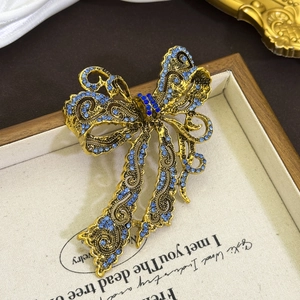 Vintage gold bow brooch with blue rhinestones displayed on an elegant jewelry tray