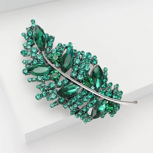Elegant feather leaf brooch with green marquise crystals on a white minimalist display stand