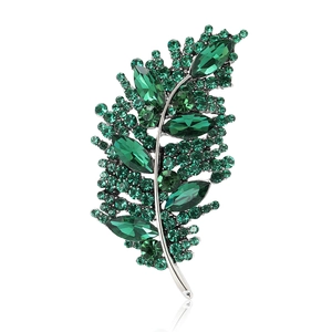 Elegant green leaf brooch with crystal rhinestones on a reflective white surface