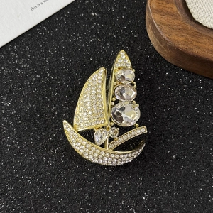 Macro detail of golden sailboat brooch with sparkling diamonds on a black background