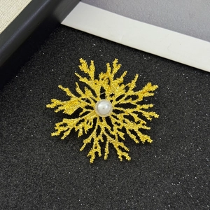 Detail of vintage gold snowflake brooch with matte texture and central pearl accent