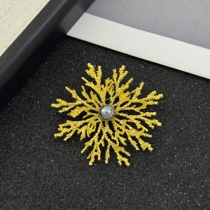 Detail view of a vintage gold-plated snowflake brooch with a grey pearl on black background