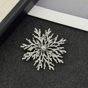 Detailed close-up of a silver snowflake brooch with a gray pearl centerpiece on a dark surface