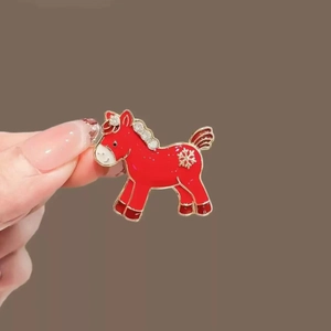 Detailed view of a red enamel horse brooch with gold trim and sparkling rhinestones