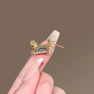Détail d'une broche crabe dorée avec pierres bleues claires sur le doigt