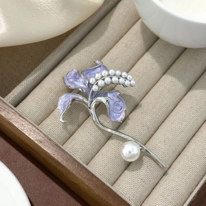Macro di una spilla a giglio in smalto viola con perle bianche su vassoio beige
