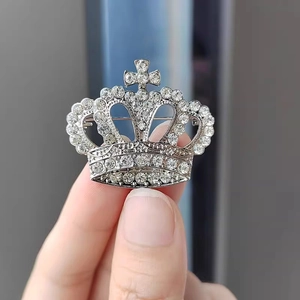 Détail d'une broche couronne argentée avec strass pavés et une petite croix