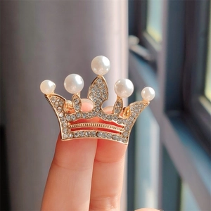 Détail de la broche couronne dorée ornée de strass brillants et de perles blanches