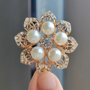 Elegant gold flower brooch featuring white crystals and pearls held by a hand