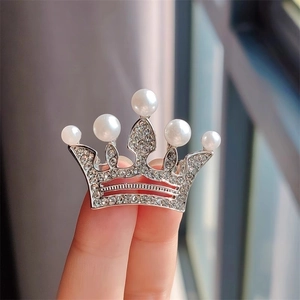 Détail d'une broche couronne argentée avec cristaux scintillants et perles blanches