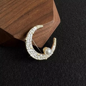 Elegant crescent moon brooch with sparkling rhinestones and a white pearl on gold metal