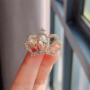 Gros plan d'une broche couronne dorée ornée de strass blancs et d'une pierre précieuse centrale