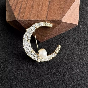 Elegant gold crescent moon brooch with sparkling rhinestones and a white pearl on black velvet