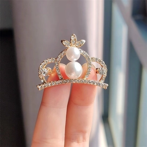 Détail d'une broche couronne dorée avec strass scintillants et perles blanches élégantes