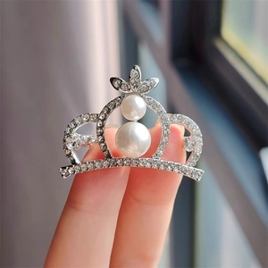 Détail de broche couronne argentée avec strass étincelants et perles blanches