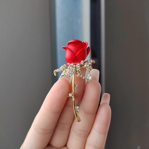 Détail d'une broche rose rouge avec des feuilles dorées et des strass étincelants