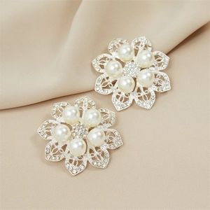 Detailed view of silver flower brooches with crystals and pearls on beige silk fabric